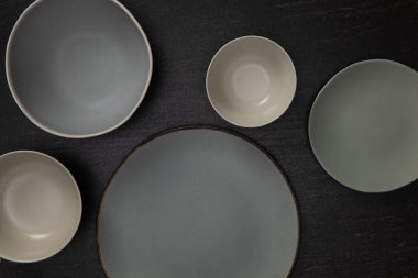 Boş seramik yuvarlak kaseler ve siyah taştan tabaklar, geleneksel el yapımı mutfak eşyaları konseptinin üst görüntüsü.