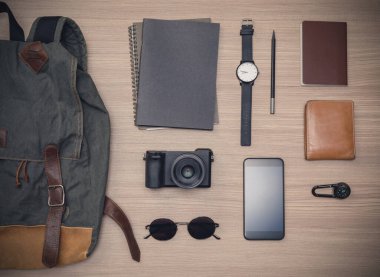 Pasaportlu gezgin aksesuarları, seyahat planları, cüzdan, kamera, kamuflaj, sırt çantası ve cep telefonu meşe ağacından ahşap masa üzerinde. Fotokopi alanı, seyahat konsepti arka planında düz uzanmış.