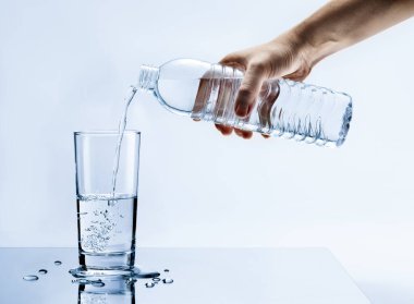 Su damlaları, sağlık hizmetleri ve güzellik hidrasyon konsepti olan temiz suyu şişeden bardağa dökerek.