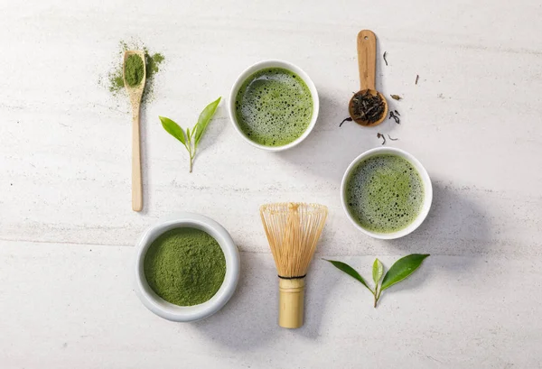 Organic matcha green tea powder in bowl with wire whisk and green tea leaf on white stone table, Organic product from the nature for healthy with traditional style