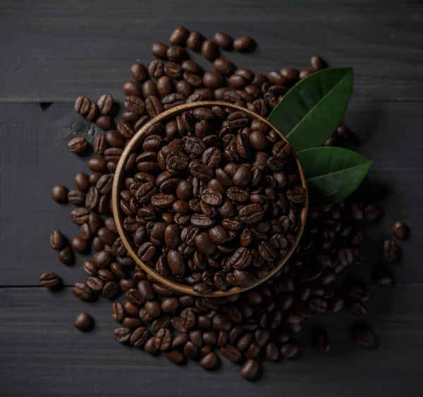 Coffee beans and coffee leaves in the bowl on the wooden table