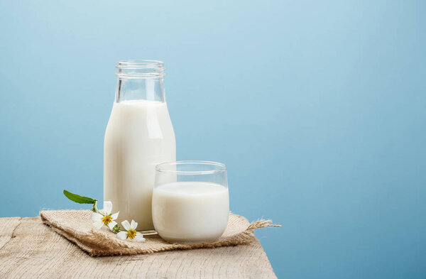A bottle of milk and glass of milk on a wooden table on a blue background