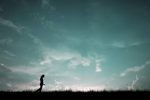 Silhouetteの若いです女の子歩く上の青い空の背景 ロイヤリティフリーのストック画像