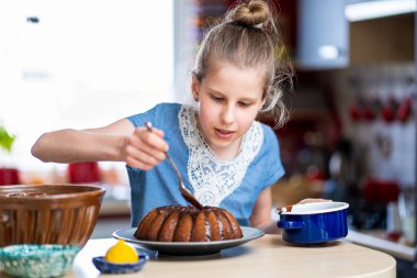 Mavi tişörtlü genç, hazırlanması kolay ve sağlıklı, ev yapımı Paskalya pastası yapıyor. Pastayı siyah çikolatayla süslüyor..