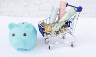 Domuz kumbarası ve alışveriş arabasındaki para beyaz masada. Kaydetme kavramı, Shope kavramı