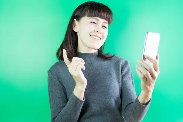 緑色の背景にスマートフォンを使用してアジアの女性の笑顔を閉じます 検索やソーシャルネットワークの概念は — ストック写真