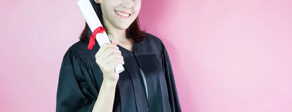 ハッピー卒業笑顔彼女ありますで卒業キャップと卒業証書で手上のピンクの背景 — ストック写真