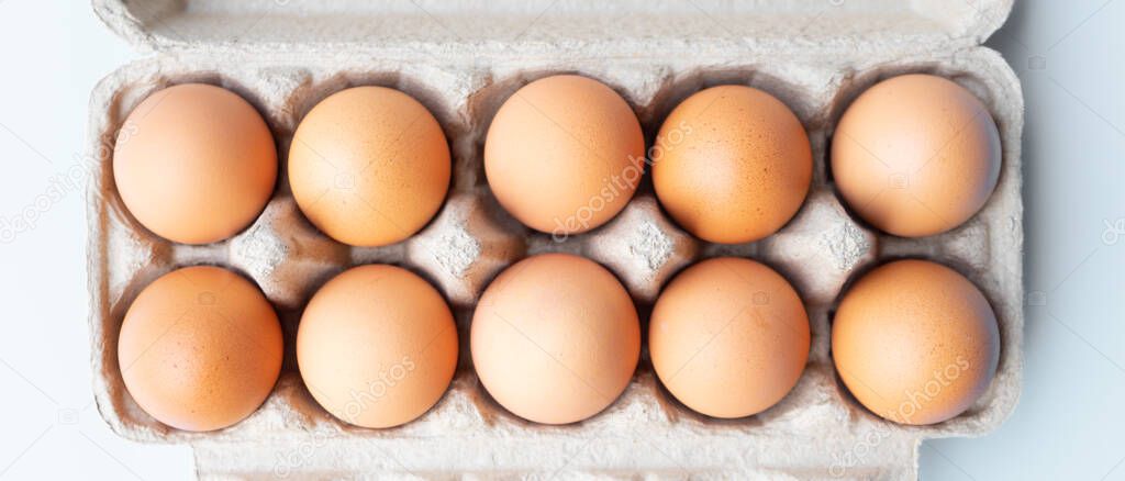 Top view chicken eggs in carton box on white wooden table.