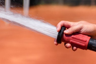 Kil tenis kortunu sularken hortumdan güçlü bir su akıntısı. Maçtan sonra kil tenis kortunun bakımı. Maç için tenis kortuna servis ve hazırlık. Yakın plan. Boşluğu kopyala