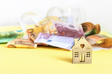 Para, bir ev ve sarı arka planda bir para kutusu. Kendi mülkünüzün ipoteği için tasarruf veya katkı payı. Aile bütçesi, hayallerin gerçek olması. Boşluğu kopyala.