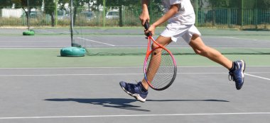 Bir çocuk tenis kortunda tenis oynar. Genç bir tenisçinin vücudu ve kortun gölgesi. Sporcu iş başında. Çocuk turnuvası maçı. Aktif spor. Boşluğu kopyala.