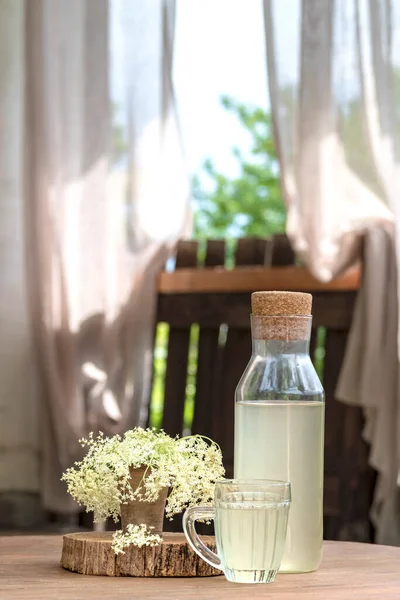 Vintage cam bir şişede ev yapımı mürver şurubu, bir bardak sambucus limonata ve ahşap bir kırsal masada mürver çiçeği. Kırsal yaşam, taşra yaşam tarzı. Doğa arasındaki çevre dostu yaşam tarzı
