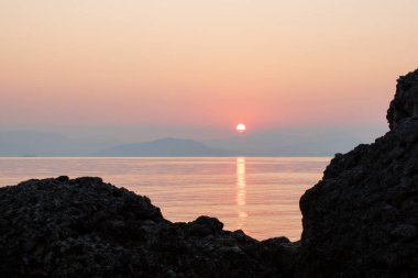 Denizin üzerinde doğal gün doğumu ve kayaların silueti. Güneş denize yansıyor, altın bir yol çiziyor. Korfu adasından Yunanistan 'a güzel bir manzara. Geçmişi. Metin için boşluk