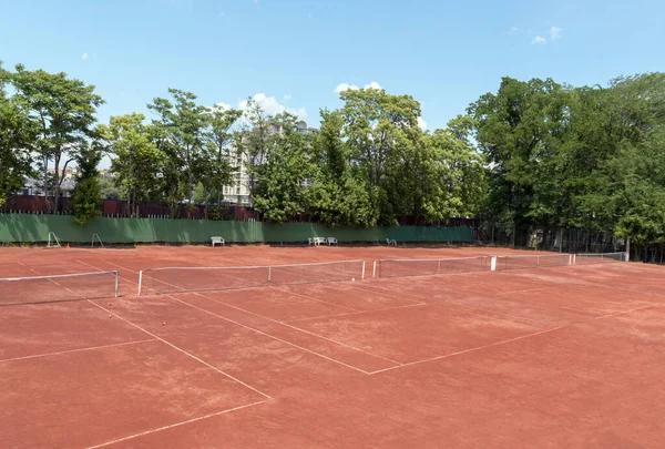 晴れた夏の日にはテニスコートを空にする 背景にある赤い粘土のテニスコート 緑の木々 青い空の上からの眺め テニスのための屋外スポーツの遊び場 テキストまたはデザインのコピースペース — ストック写真