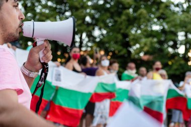 Filibe, Bulgaristan Temmuz - 10.2020: Yolsuzluk ve yetkinin kötüye kullanılmasını protesto eden sözcü, koruyucu maskeli bir grup insan ve arka planda Bulgar bayrağı bulanık. Seçici odak