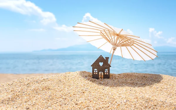 Güneş şemsiyesi ve kumlu sahildeki ev, arka planda mavi gökyüzü ve deniz. Tatil köyü gayrimenkul konseptine yatırım. Denizde rüya tatili. Boşluğu kopyala.