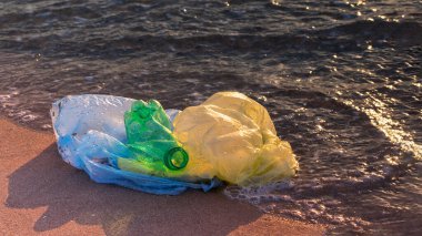 Plastik şişe ve torbalar şafağın altın ışığında kıyıya yakın deniz suyunda. Dünya okyanusu kirliliği. Ekoloji. Çevre koruma. Seçici odak, boşluğu kopyala