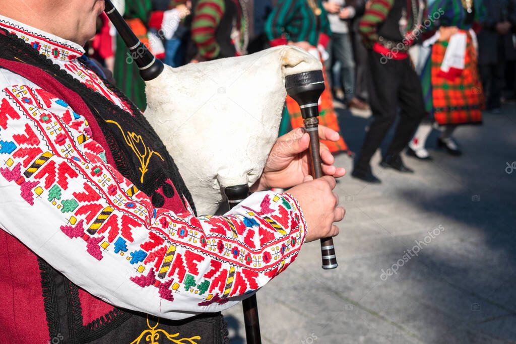 Man in traditional national Bulgarian costume with embroidered patterns plays ancient musical folk wooden wind instrument - bagpipes in Plovdiv, Bulgaria.