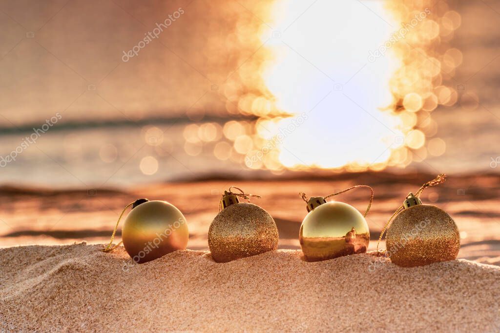 Christmas toys - golden balls on the beach, blurred sea in sunset light in the background. New Year or Christmas card, invitation with copy space for text