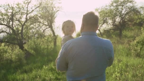 Papa porte sa fille de 2 ans dans ses bras dans le jardin, Bonne petite fille souriante . — Video