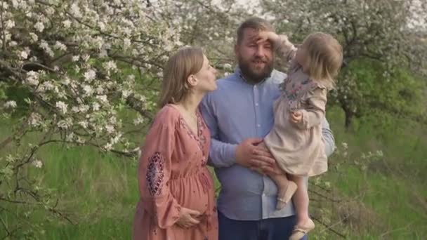 Lycklig familj tillsammans i aprilträdgården, nära blommande träd. Dottern smeker försiktigt pappans huvud — Stockvideo