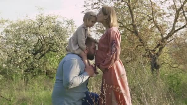 Vader houdt zijn 2-jarige dochter op zijn schouders en kust de buik van zijn zwangere vrouw, — Stockvideo