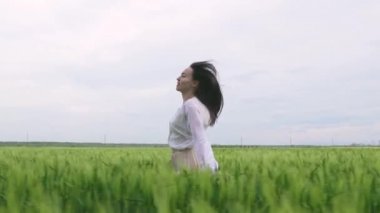 Güzel, beyaz tişörtlü ve etekli beyaz saçlı beyaz bir kız gün batımında buğday tarlasında koşar ve kameraya gülümser.
