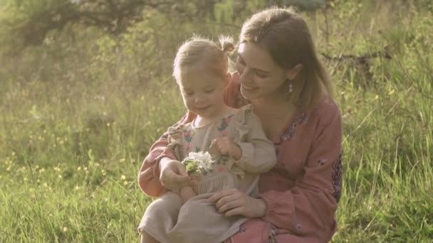 La madre embarazada y su hija en un vestido bordado juegan con una flor en el jardín , — Vídeos de Stock