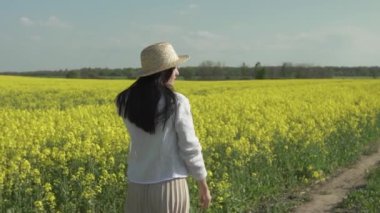 Hasır şapkalı genç mutlu kadın sarı bir tarlada yürüyor ve güneşin tadını çıkarıyor.