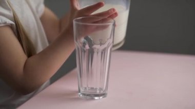 Yan manzara, beyaz küçük kız bardağa süt döker.