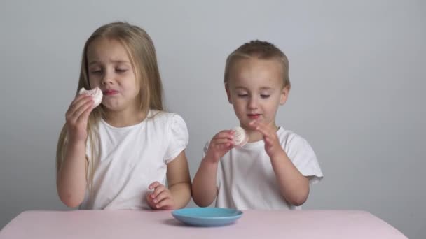 Caucasian little brother and sister in white T-shirts with white hair eating macaroons, — Stock Video