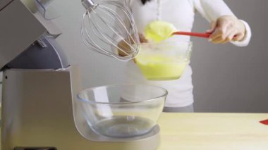 Mutfaktaki kız mikserin cam kasesine spatula ve muhallebi atıyor..