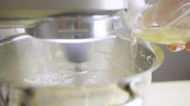 Yakın plan. Mutfaktaki kız mutfak makinesinde krem şanti yapıyor. Kadın kremaya jelatin döker.