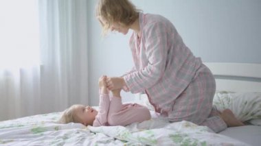 Yatakta pijama giymiş hamile bir anne kızının bacaklarını öper..