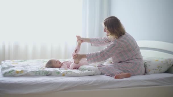 La ragazzina salta sul letto. Mamma e figlia giocare e divertirsi in camera da letto. — Video Stock