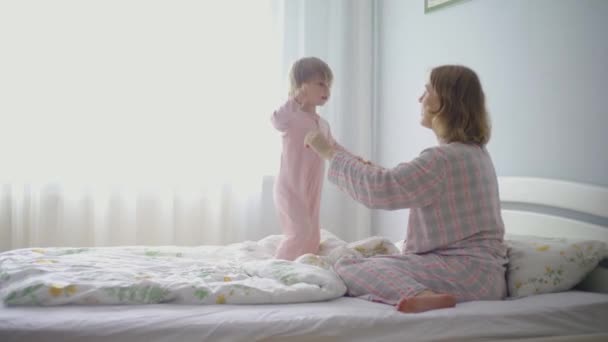 Kleines Mädchen umarmt ihre schwangere Mutter. Mutter und Baby im Schlafzimmer auf dem Bett. — Stockvideo