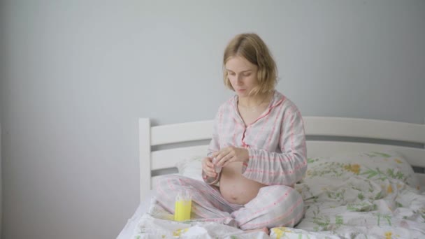 Uma mulher grávida toma comprimidos e bebe água. Uma mulher grávida de pijama está tomando vitaminas . — Vídeo de Stock