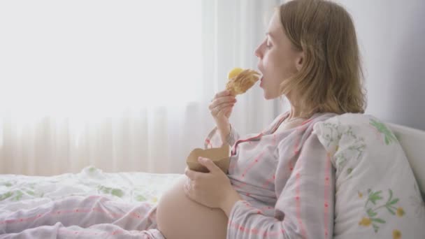 Close-up. mulher grávida em pijama na cama come um croissant com eco utensílios — Vídeo de Stock