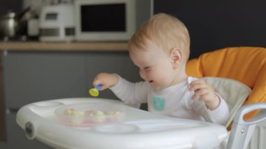 Yakın plan. Bebek beslenme koltuğunda oturuyor, gülümsüyor ve kaşıkla oynuyor..