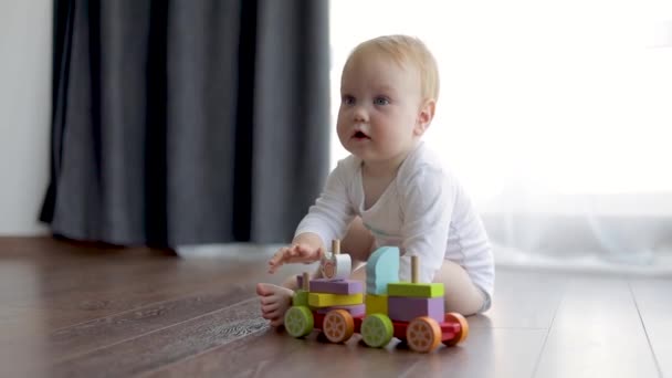 Малыш играет с деревянным поездом на полу . — стоковое видео