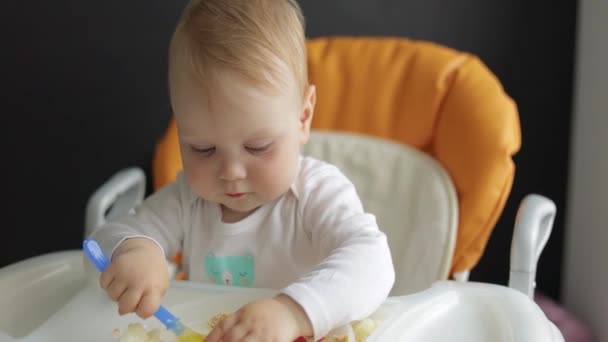 正面図。肖像画。小さな男の子は餌やりの椅子で赤ちゃんの食べ物を食べる. — ストック動画