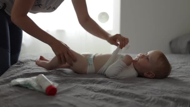 Vista lateral. Mãe muda fraldas para bebês na cama — Vídeo de Stock