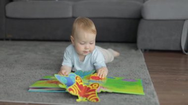 Neşeli bebek halıya uzanıp kitap okuyor.