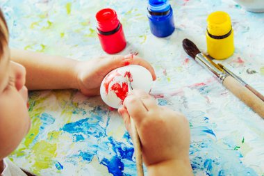 Çocuk Paskalya tarafından kırmızı boya ve boya yumurtası ile bir fırça tutar, 