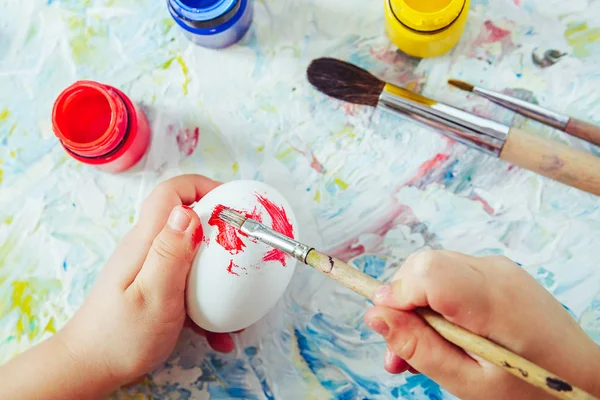 Handen van het kind houden een penseel met rode verf en verf ei door Rechtenvrije Stockafbeeldingen