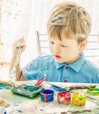 Çocuk bir sanat fırçası elinde tutar ve bir woode üzerinde boya çizer