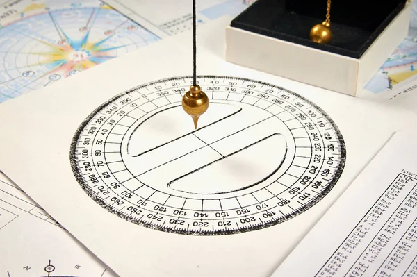 Astrological pendulum for tarot and astrological circle on the background of astrological charts and horoscopes