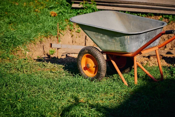 Garden work and tools. A metal garden wheelbarrow stands on a green lawn next to a dug place