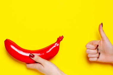 Sarı arka planda kırmızıya boyanmış muz resmi. Kırmızı muz ve işaret parmağı sarı arka planda..