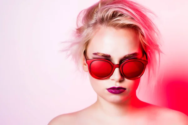 Model Russian blonde with a short haircut in red glasses and a bright top layout closeup on a pink background.